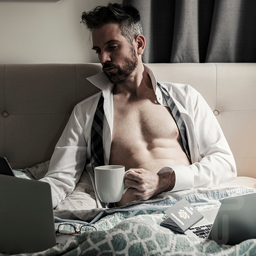 Handsome man with his shirt open working on his computer and holding a mug loose tie around his neck