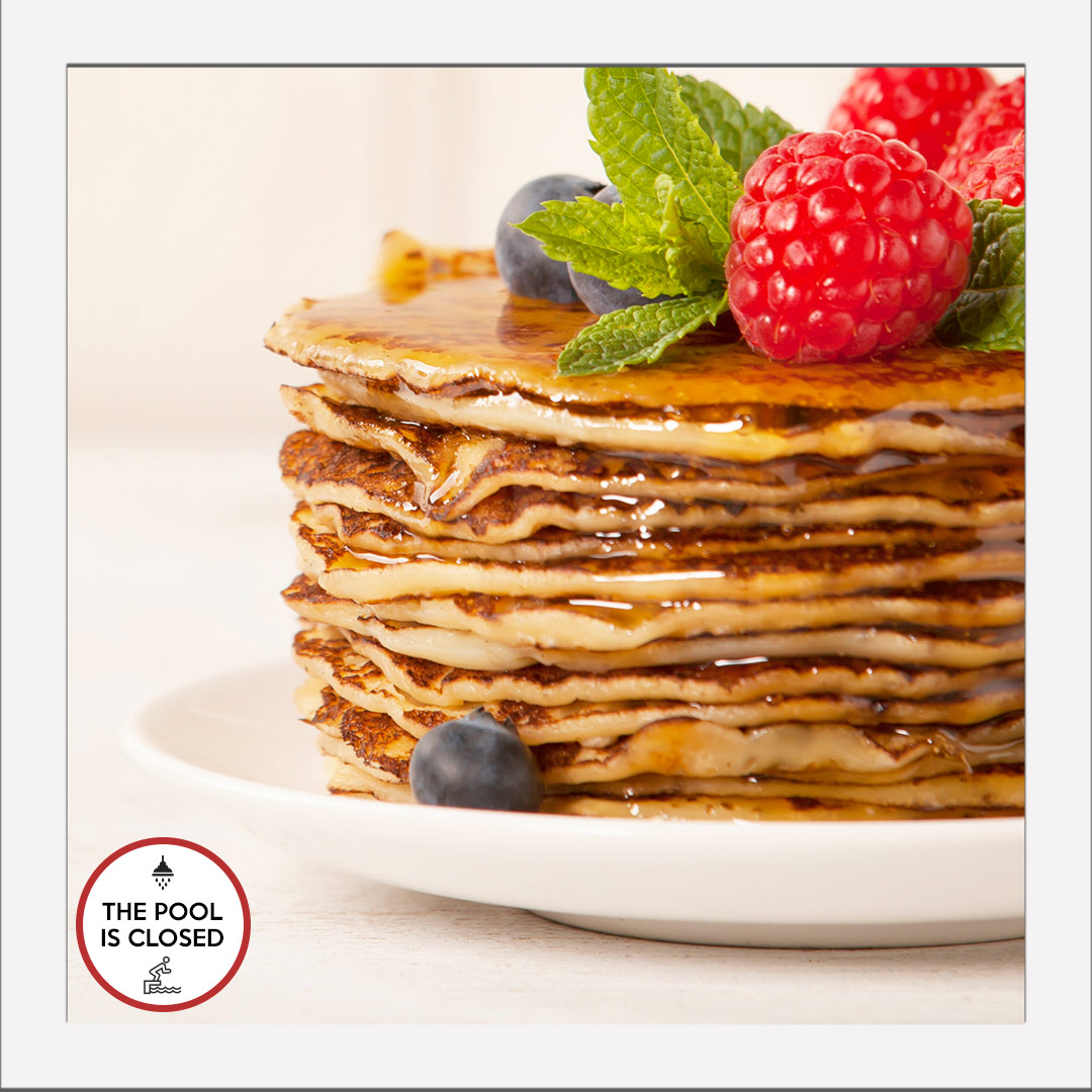 Stack of pancakes covered in syrup, raspberries, blueberries and sprigs of mint leaves.